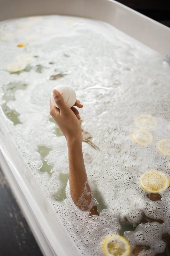 Unrecognizable woman holding bath bomb in water with foam